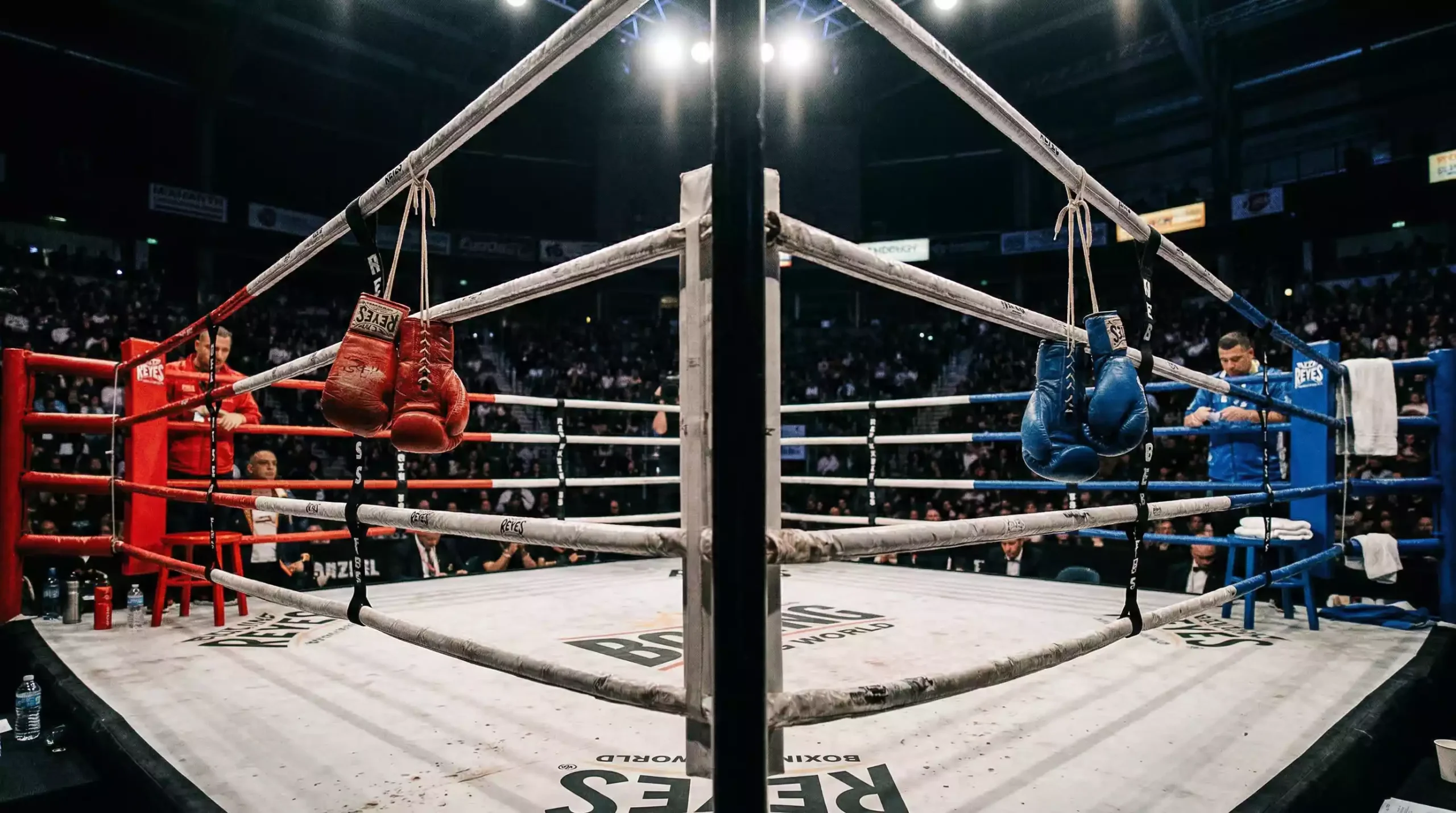 Dos esquinas opuestas de un ring de boxeo con guantes rojo y azul colgados de las cuerdas