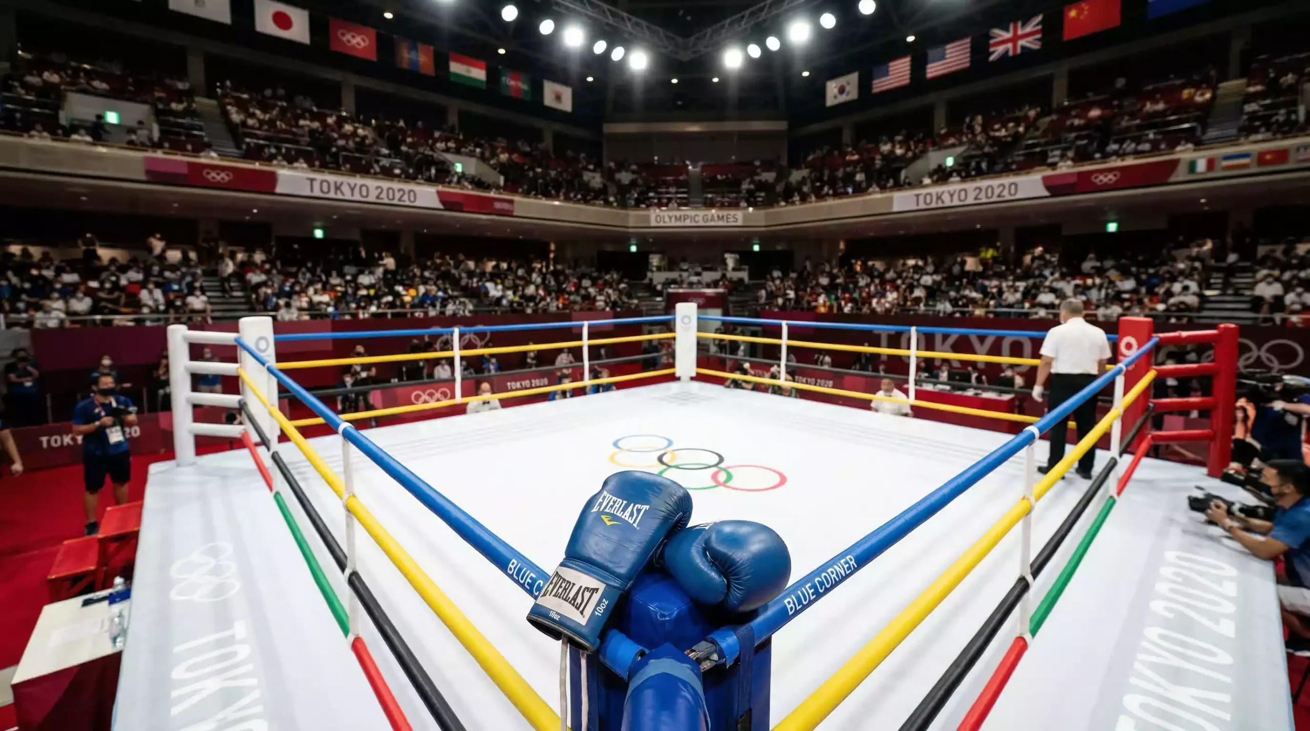 Ring de boxeo con cuerdas olímpicas de colores y un par de guantes de boxeo azules sobre la esquina
