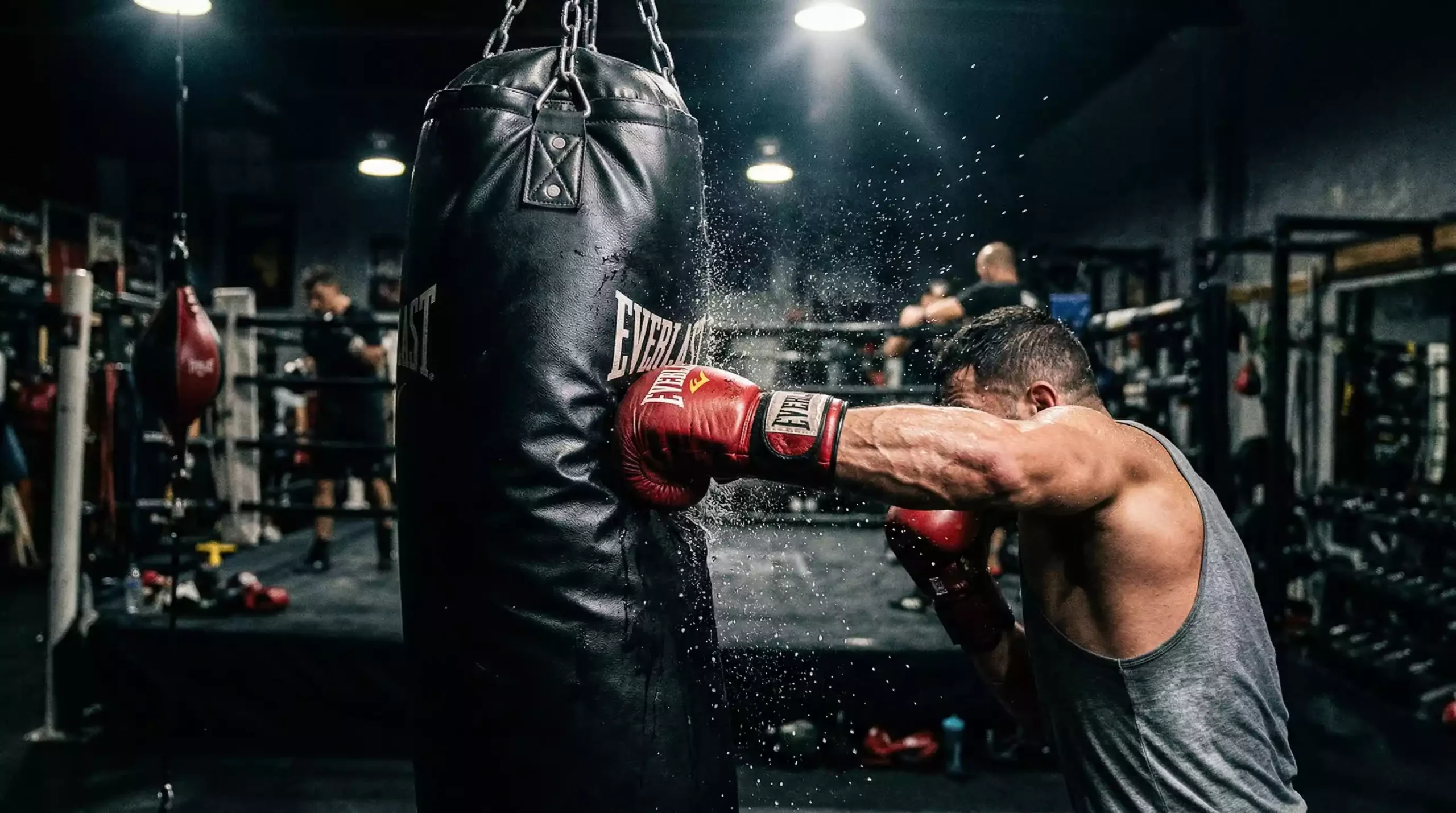 Guante de boxeo rojo impactando un saco de entrenamiento en un gimnasio profesional con iluminación cenital