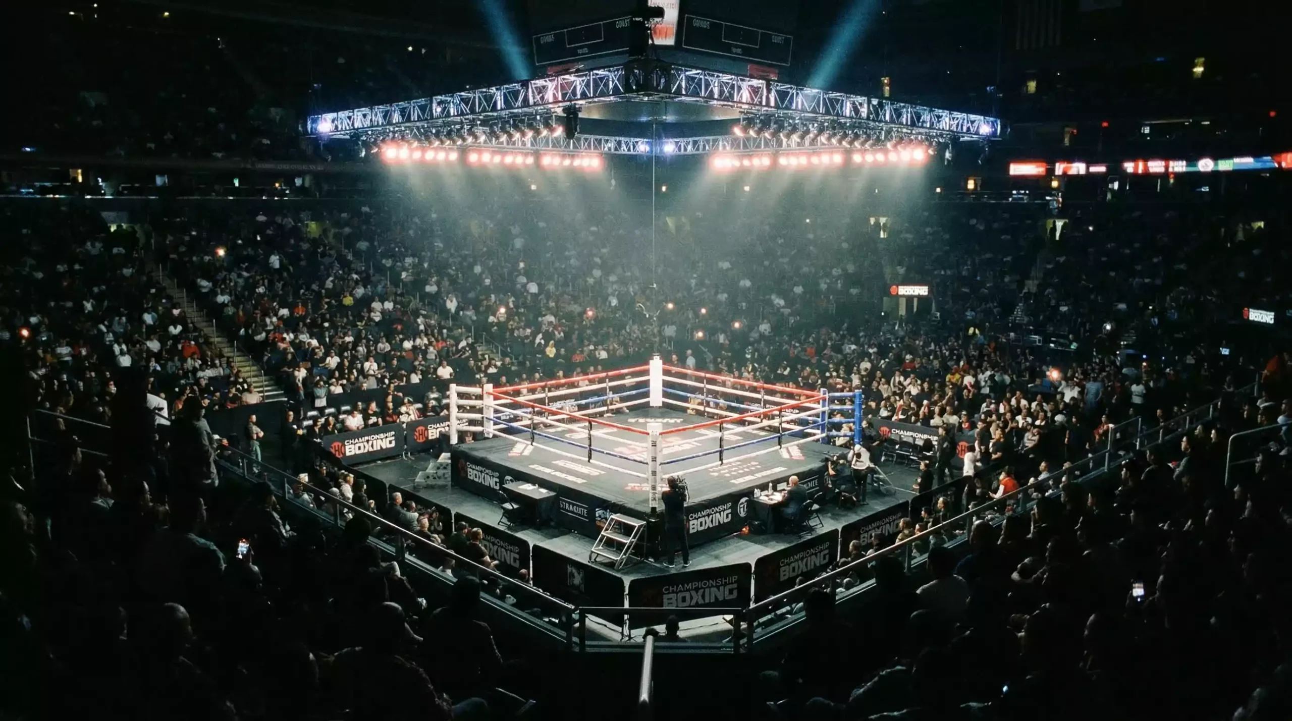 Ring de boxeo iluminado visto desde las gradas antes del inicio de un combate nocturno
