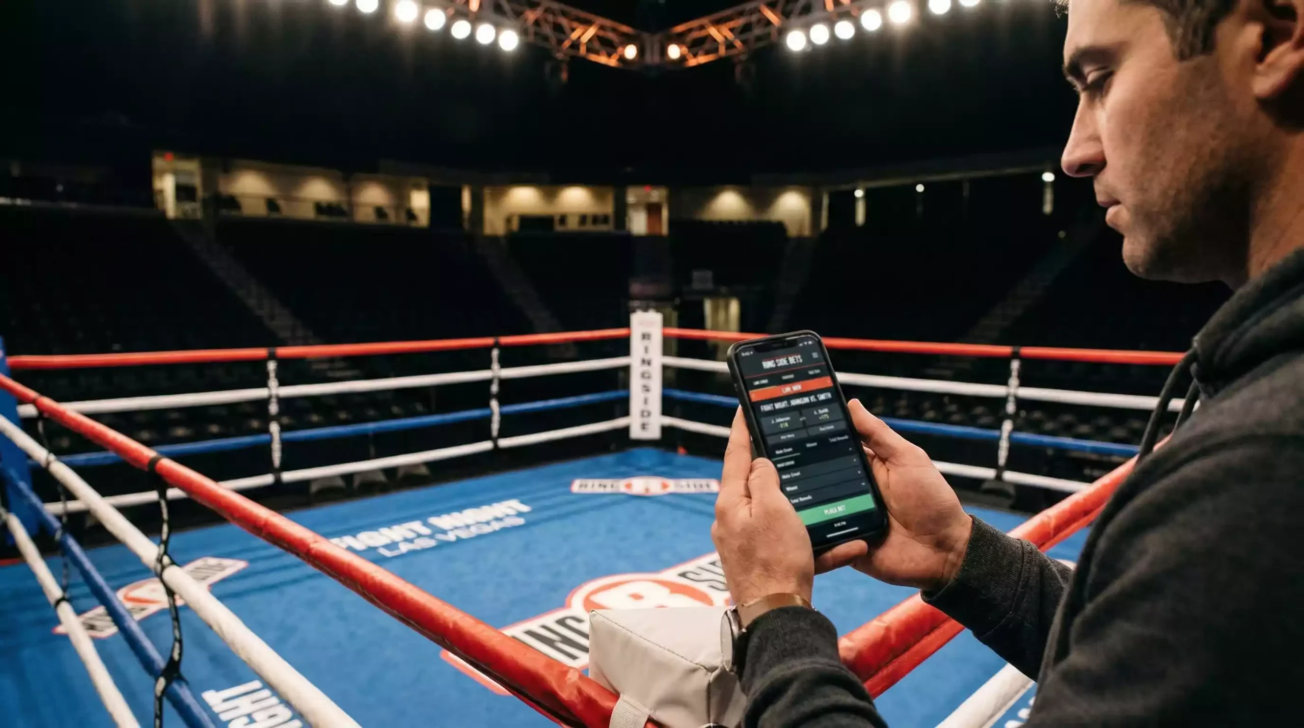 Persona usando un teléfono móvil frente a un ring de boxeo vacío con cuerdas rojas y azules