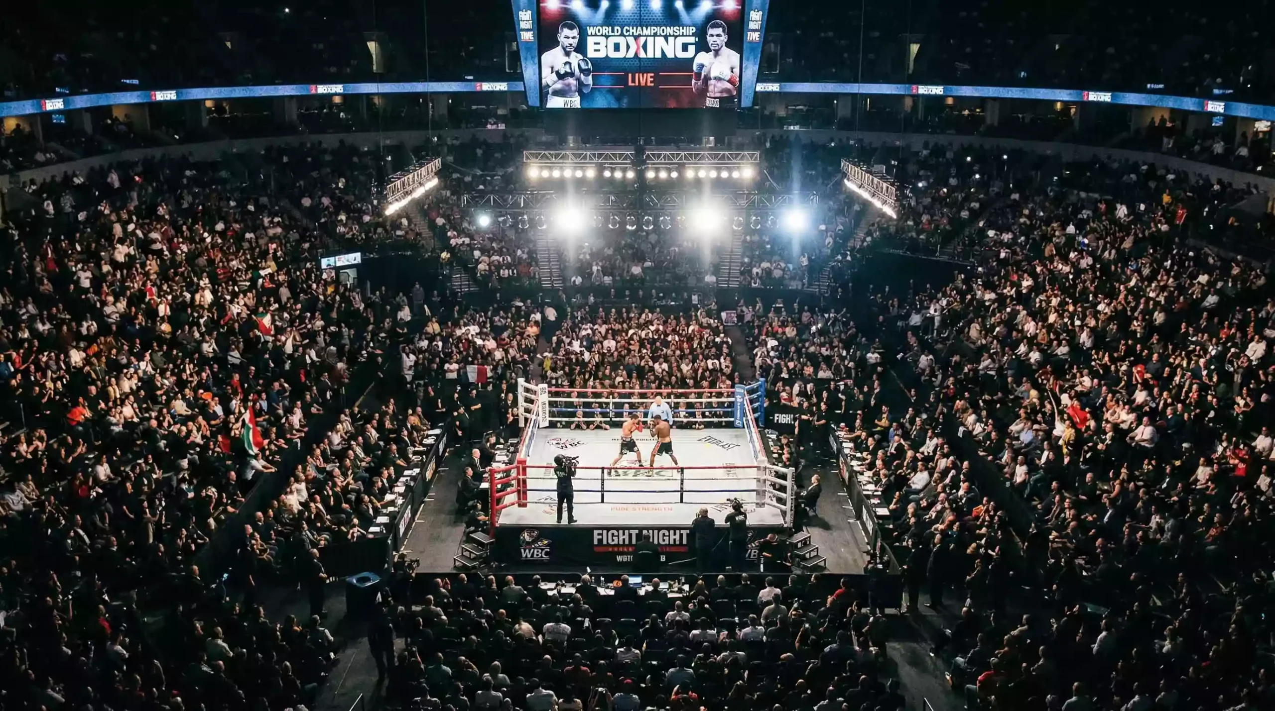 Ring de boxeo profesional visto desde arriba con focos encendidos en una arena llena de espectadores